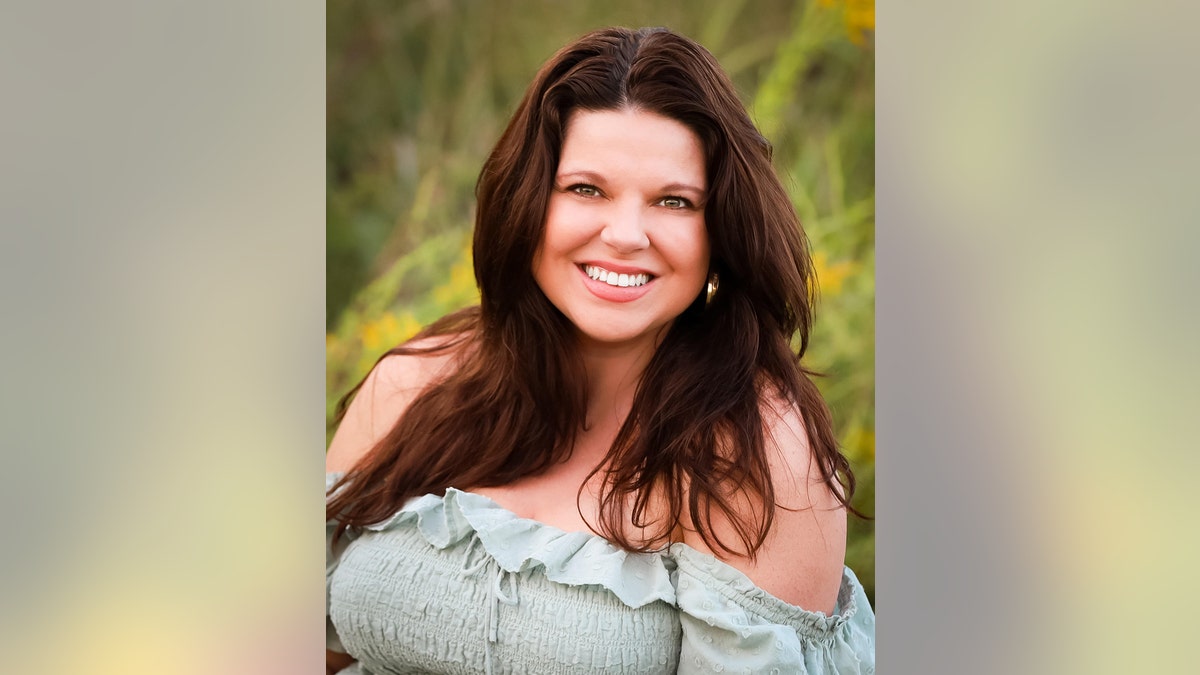 Крупный план улыбающейся Эми Даггар Кинг в светло-зеленом платье с открытыми плечами в поле.