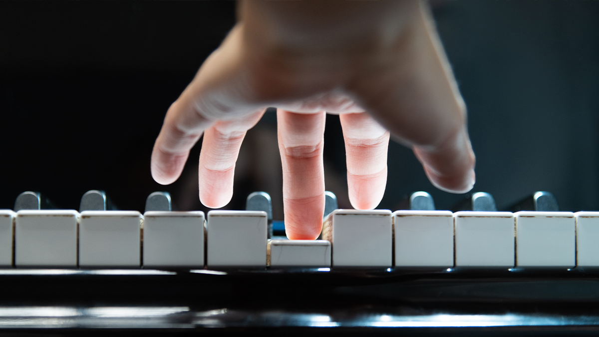 Рука над клавиатурой фортепиано, нажимает на клавишу средним пальцем